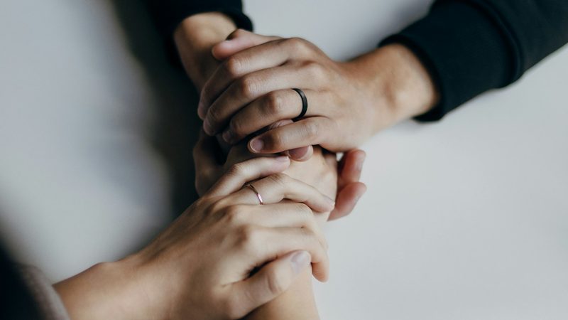 Two people hold each other’s hands across a table in support