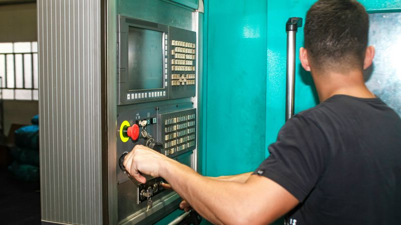 A machinist works the control panel of a CNC machine