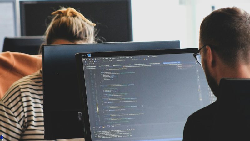 Two developers at their desks, one screen full of code