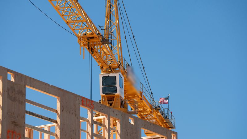 A yellow tower crane with its operator cab rises over a wood-frame building under construction