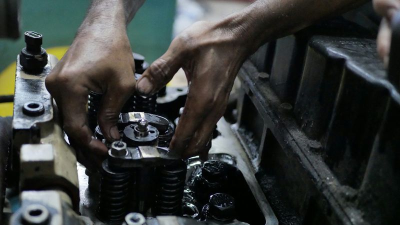 A mechanic's hands work on the valve springs of an engine