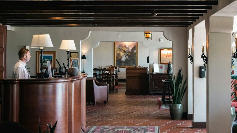 A receptionist stands behind the front desk in the lobby of a hotel