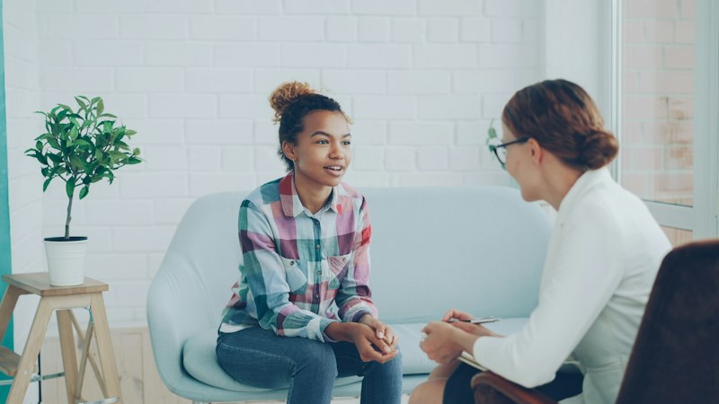 A young woman on a sofa talks with a staff member who takes notes on a notepad