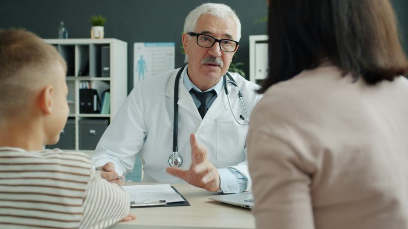 A doctor talks across his desk with a mother and her son in a clinic office