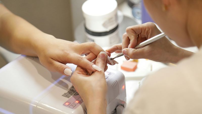 A nail technician works on a client's nails at a salon table