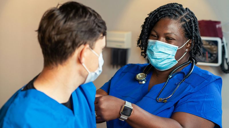 Two nurses in blue scrubs and face masks, one with a stethoscope round her neck