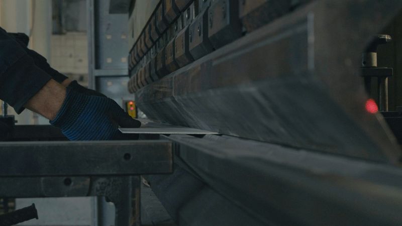Gloved hands feed a sheet of metal into a press brake to be bent