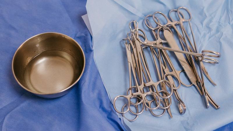 Clamps, scissors and a scalpel handle laid out on a blue sterile wrap beside a steel bowl